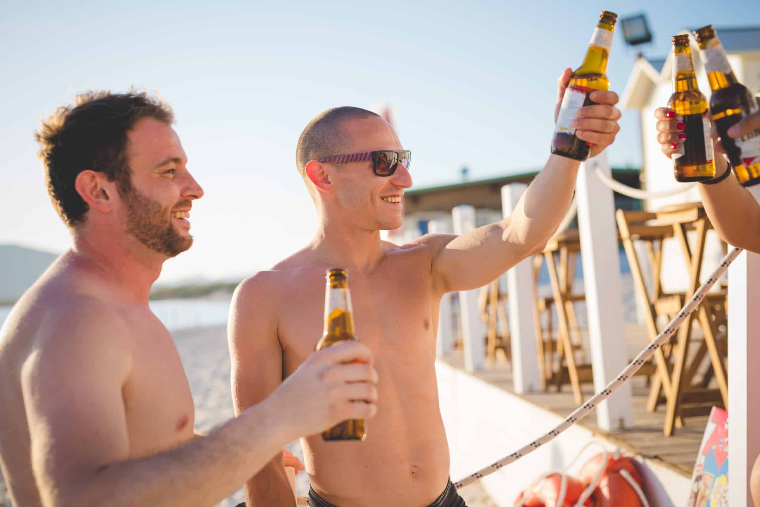 group of young multiethnic friends women and men at the beach in summertime toasting with some beers in a beach bar - friendship, relaxing, happy hour concepts